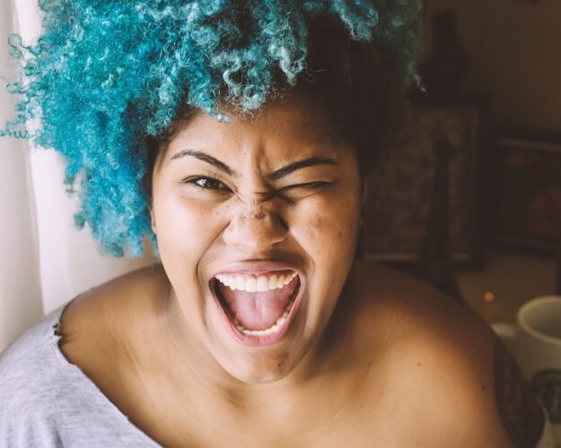 Getinte vrouw met blauw haar die een stralende glimlach heeft met witte tanden